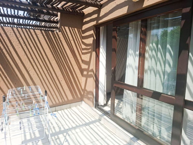 A private balcony featuring tiled flooring, a timber pergola overhead, and a large sliding glass door providing access to the interior.