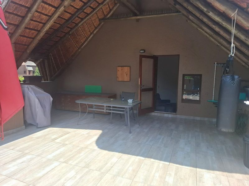 Covered outdoor patio area featuring a traditional thatched roof with exposed timber rafters and modern tiled flooring, providing a versatile space for relaxation.