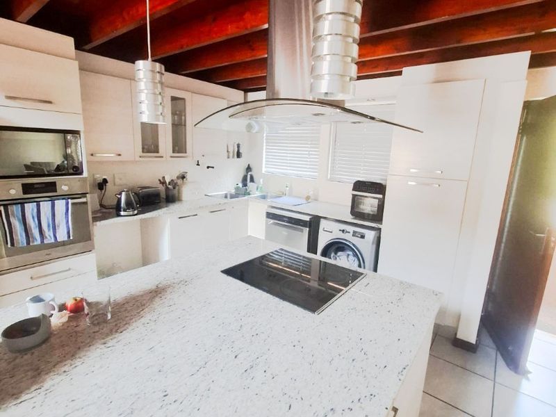 Modern kitchen featuring granite countertops, built-in appliances, and striking exposed timber ceiling beams, offering a functional and stylish culinary space.