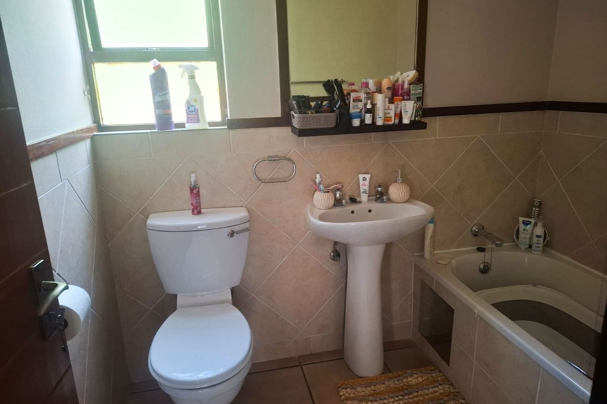 A functional bathroom featuring a pedestal basin, toilet, and built-in bathtub with neutral wall and floor tiling.