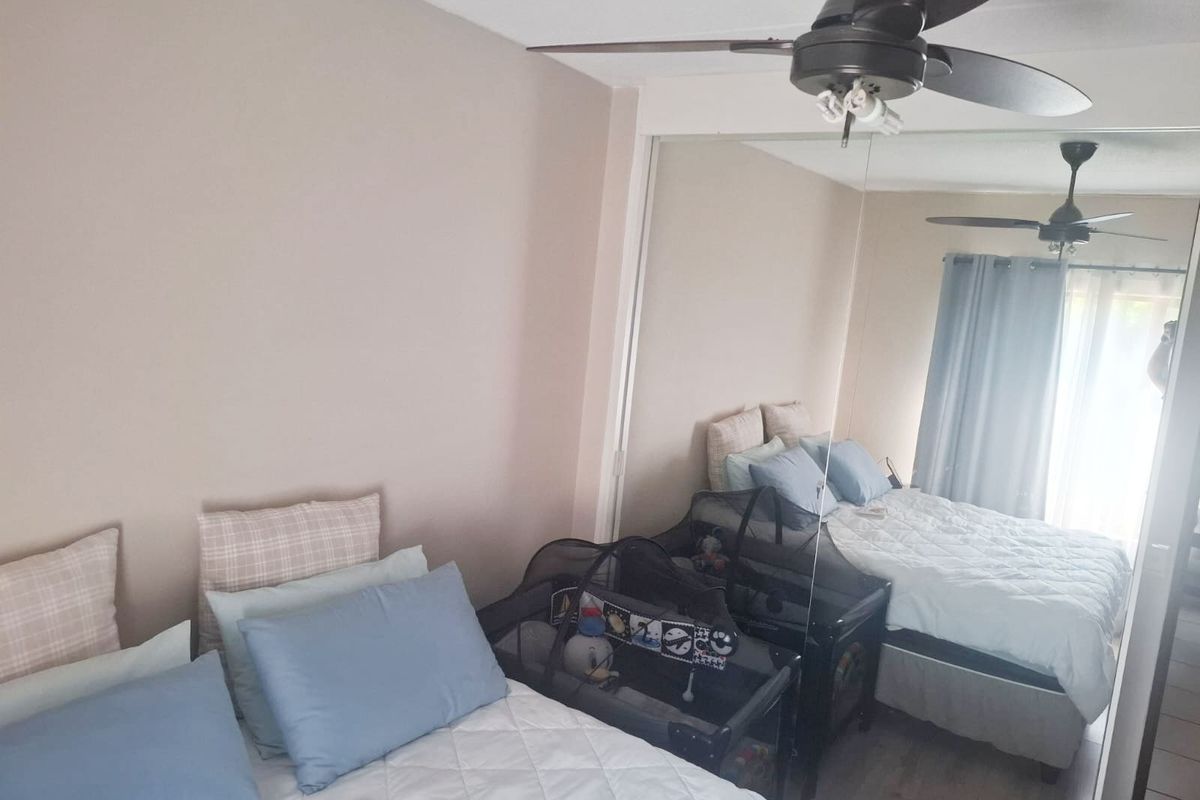 A bedroom featuring a ceiling fan and large mirrored sliding wardrobe doors, providing ample storage and reflecting natural light into the space.