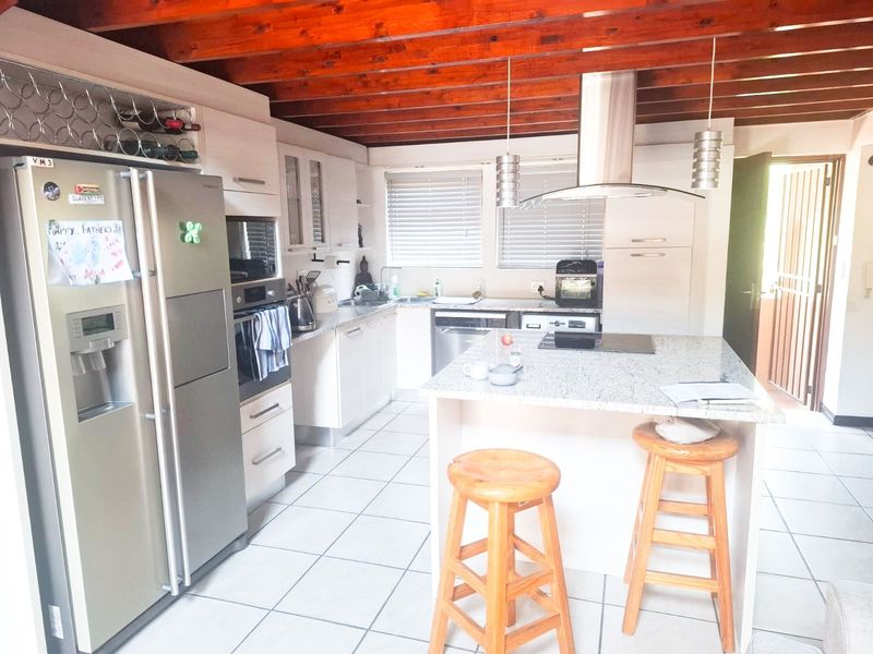 Modern kitchen featuring a central island with granite countertops, built-in appliances, ample cabinetry, and distinctive exposed timber ceiling beams.