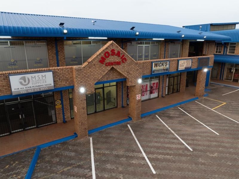Aerial view of the Mosaic Centre commercial property featuring a brick facade, metal roofing, and a paved parking area with multiple storefronts.