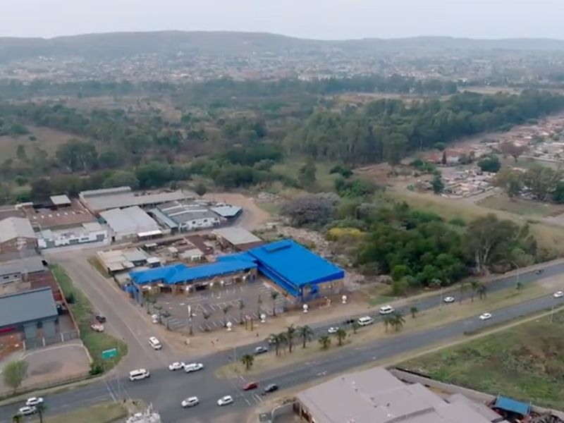 Aerial view of a commercial property featuring a blue-roofed building with an adjacent asphalt parking area, situated near a main road.