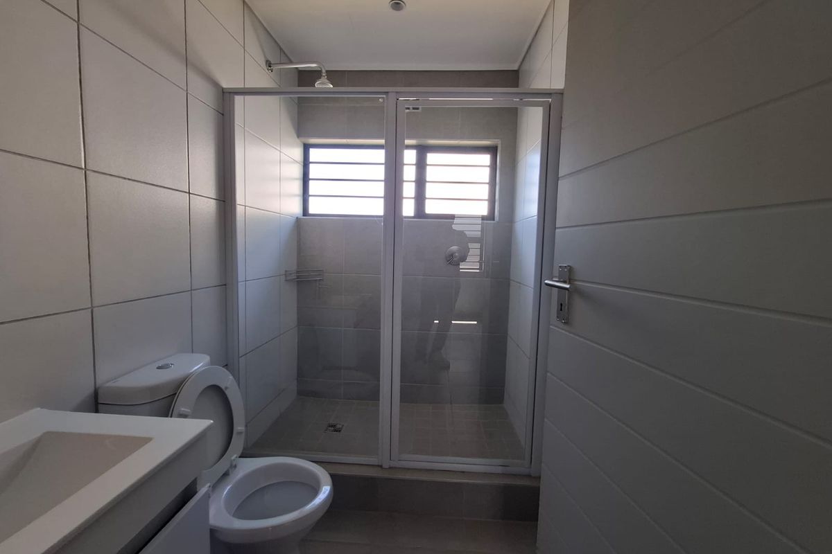 A clean, modern bathroom featuring a glass-enclosed shower, a white vanity basin, and neutral wall and floor tiling.