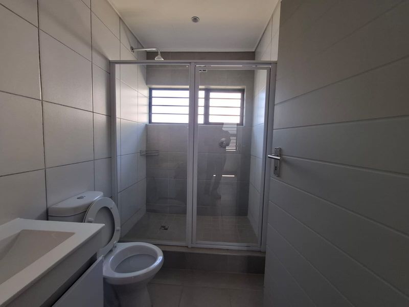 A clean, modern bathroom featuring a glass-enclosed shower, a white vanity basin, and neutral wall and floor tiling.