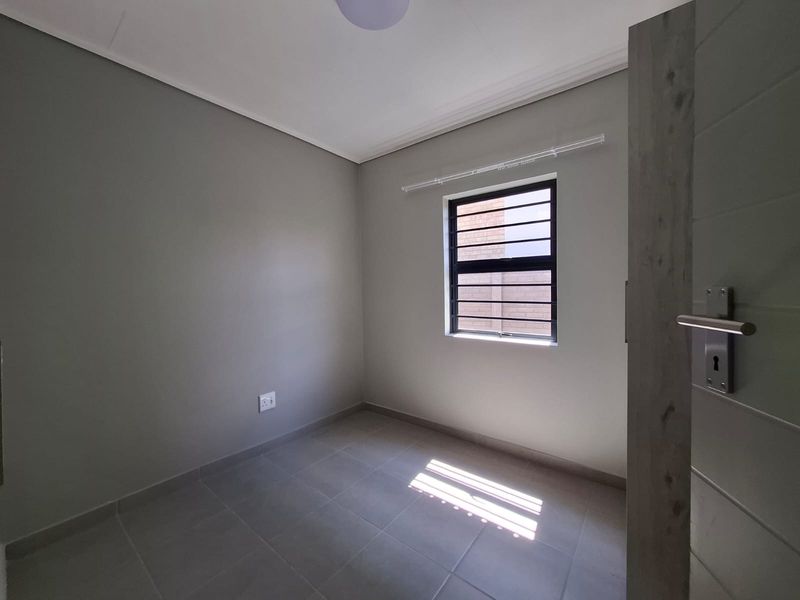 A clean, empty bedroom featuring neutral grey walls, tiled flooring, and a window fitted with security bars.