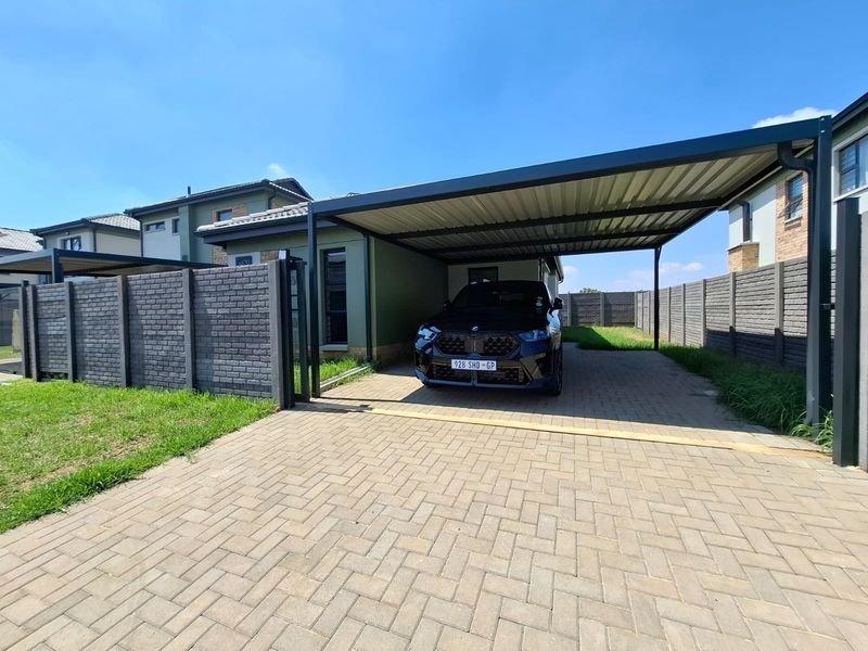 A modern residential exterior featuring a paved driveway, a spacious metal-roofed carport, and secure precast concrete perimeter walling.