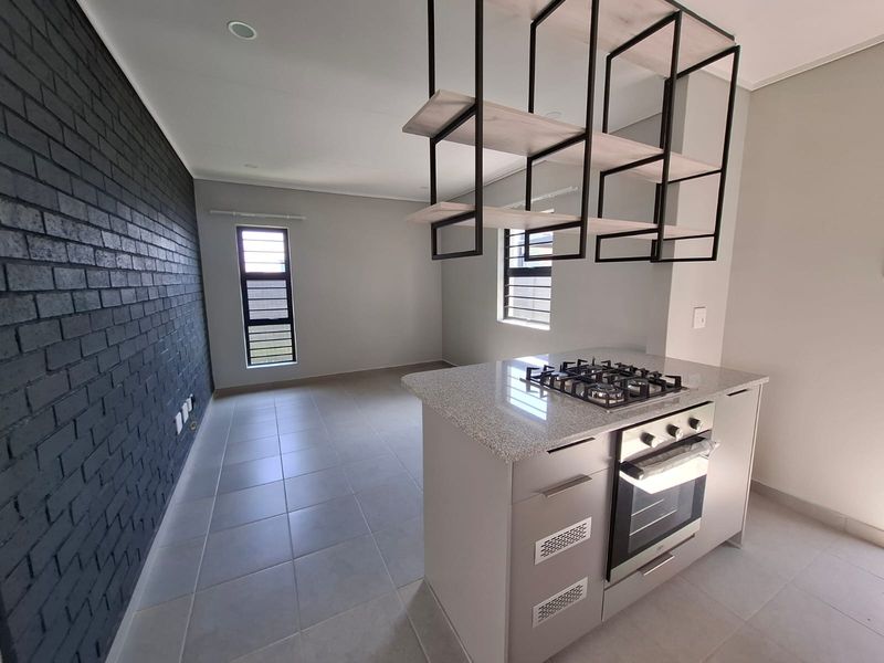 Modern kitchen featuring a central island with built-in oven and gas hob, complemented by a striking black brick feature wall and suspended shelving.