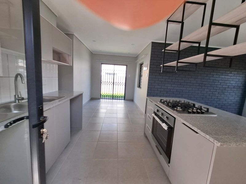Modern kitchen featuring sleek cabinetry, stone countertops, a gas hob with built-in oven, and a stylish exposed brick feature wall with suspended shelving.