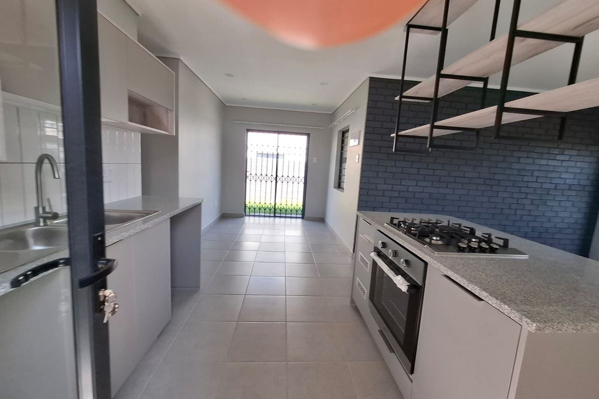 Modern kitchen featuring sleek cabinetry, stone countertops, a gas hob with built-in oven, and a stylish exposed brick feature wall with suspended shelving.
