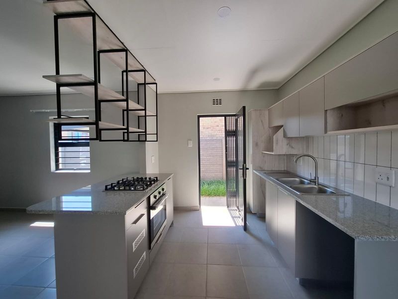 Modern kitchen featuring granite countertops, built-in oven, gas hob, stainless steel sink, and stylish overhead shelving, leading out to a private rear courtyard.
