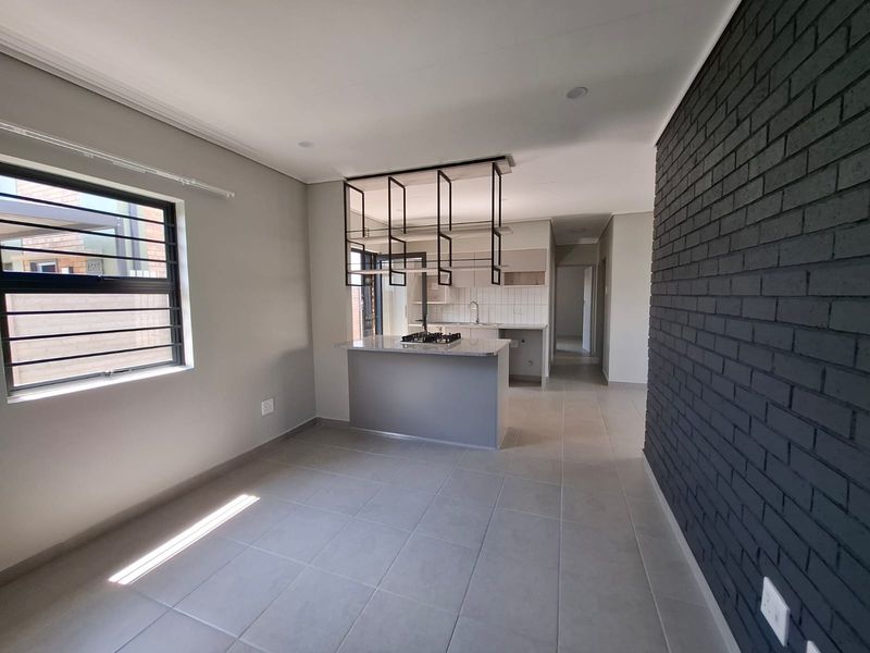 Modern open-plan kitchen featuring a central island with gas hob, suspended shelving, and a striking dark exposed brick feature wall.