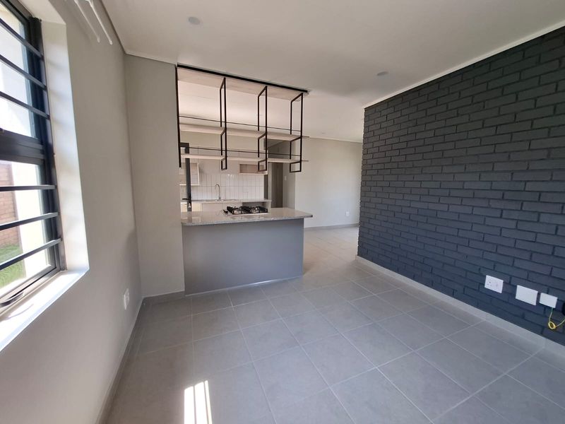 Modern open-plan living area featuring a kitchen with gas hob, granite countertops, and a striking dark grey exposed brick feature wall.