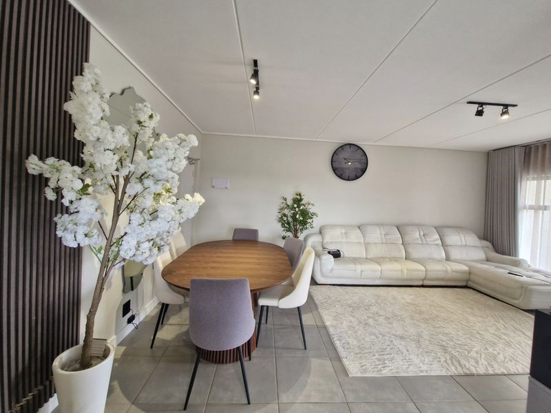 An open-plan living and dining area featuring neutral tiled flooring, modern track lighting, and decorative slatted wall paneling.