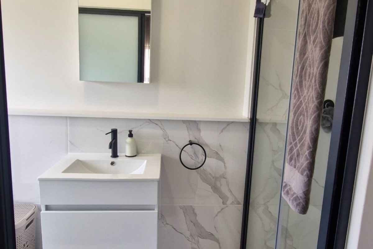 Modern bathroom featuring a wall-mounted vanity with a black mixer tap, marble-look wall tiling, and a glass shower enclosure with a black frame.