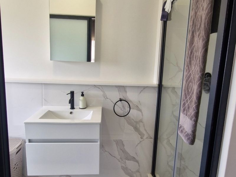 Modern bathroom featuring a wall-mounted vanity with a black mixer tap, marble-look wall tiling, and a glass shower enclosure with a black frame.