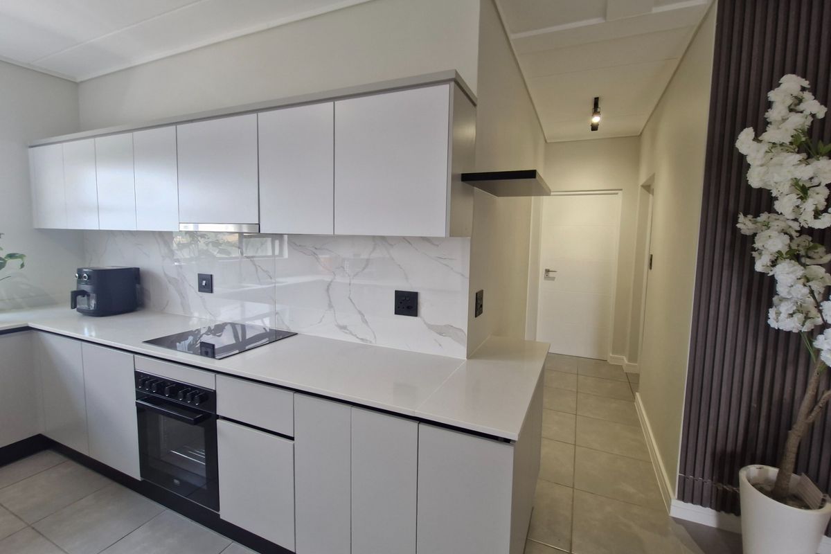 Modern kitchen featuring sleek white cabinetry, stone countertops, marble-look splashback, and integrated appliances, complemented by neutral tiled flooring.