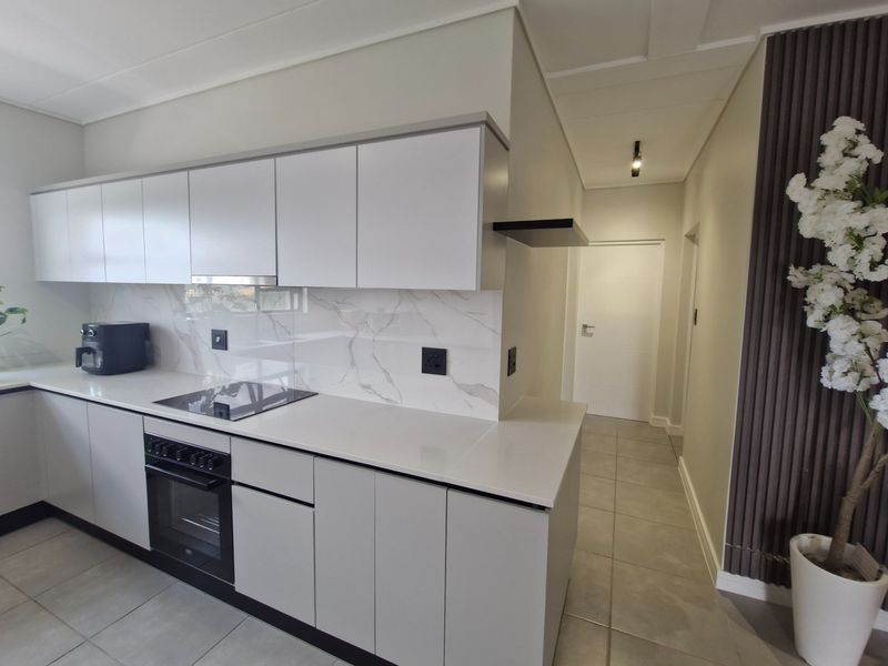 Modern kitchen featuring sleek white cabinetry, stone countertops, marble-look splashback, and integrated appliances, complemented by neutral tiled flooring.