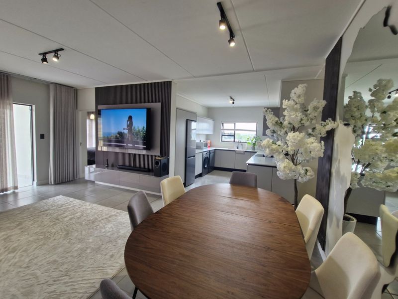Modern open-plan living area featuring a sleek slatted feature wall, contemporary kitchen with built-in appliances, and neutral tiled flooring throughout.