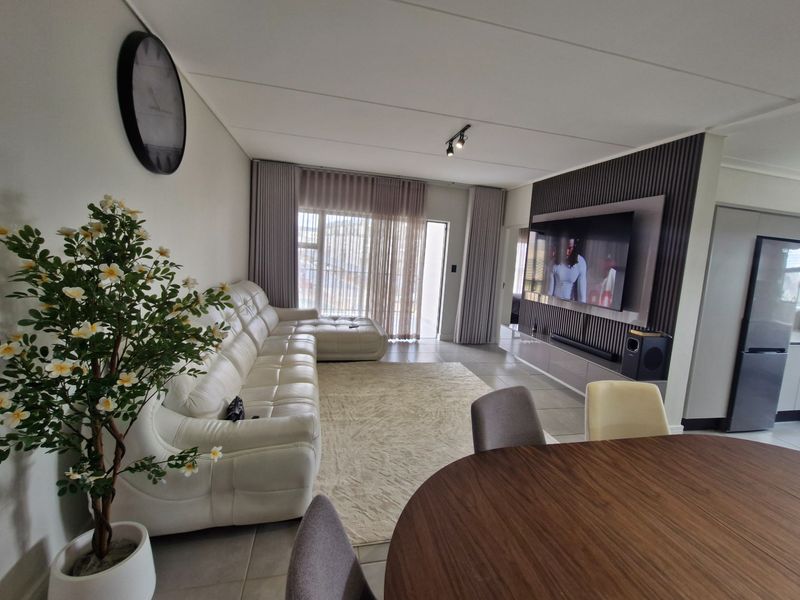Modern open-plan living area featuring tiled floors, a contemporary slatted feature wall with integrated media console, and large sliding doors leading to the exterior.