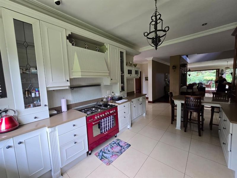 Spacious kitchen featuring classic white cabinetry, a prominent red gas stove, tiled flooring, and an open-plan layout flowing into the dining area.