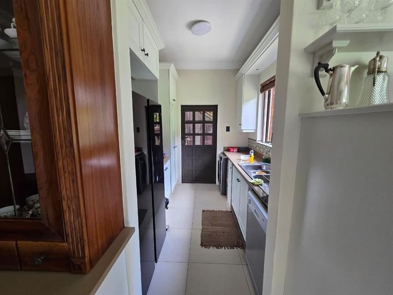 A functional scullery area featuring built-in cabinetry, a double basin sink, and tiled flooring, providing convenient additional workspace and storage.