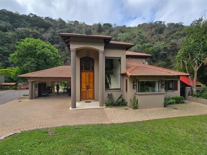 A well-maintained front elevation of a modern house featuring a tiled roof, paved driveway, covered carport, and an impressive double wooden entrance door.