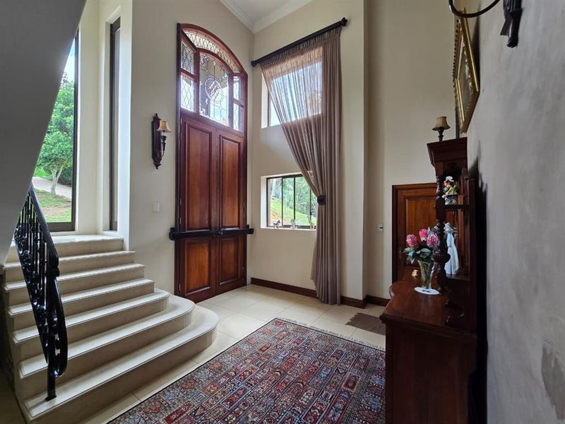 Grand entrance foyer featuring high ceilings, tiled flooring, a feature timber front door with leadlight glass, and a decorative wrought iron staircase.