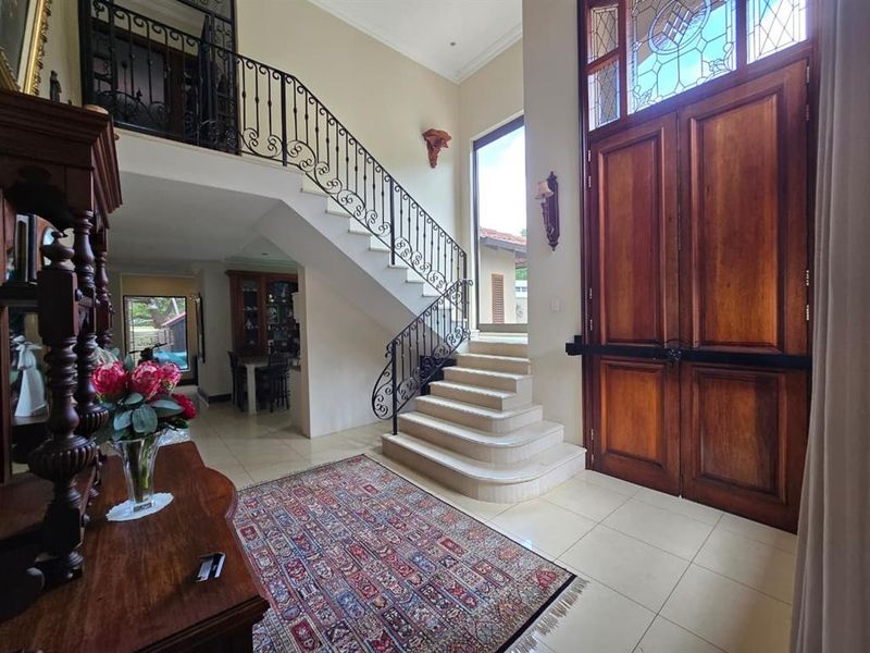 Grand entrance hall featuring a stone staircase with ornate wrought iron railings, double wooden doors, and high ceilings with stained glass detailing.