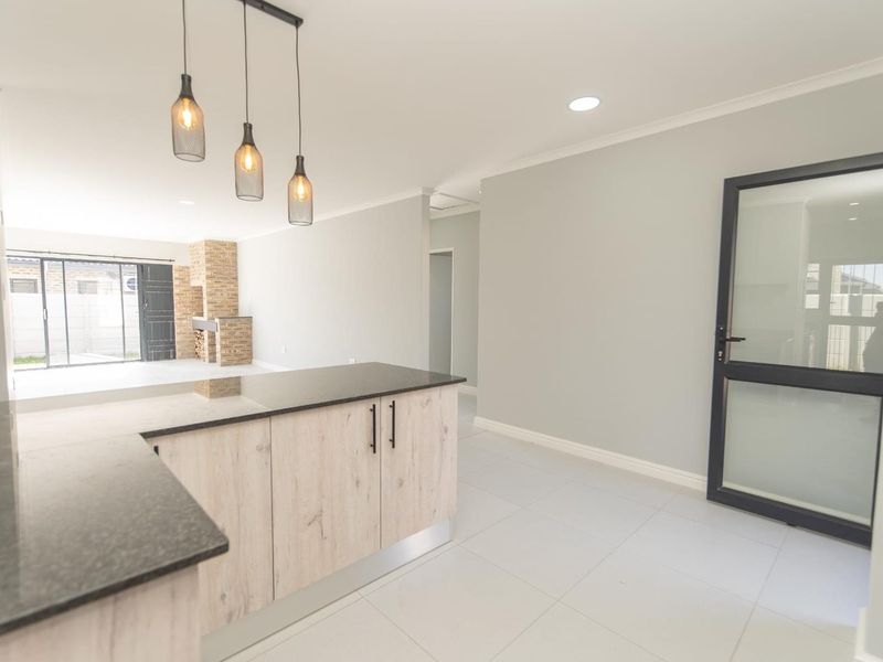 Modern open-plan living area featuring a kitchen island with granite countertops, tiled flooring, and a brick fireplace, leading to an outdoor patio space.