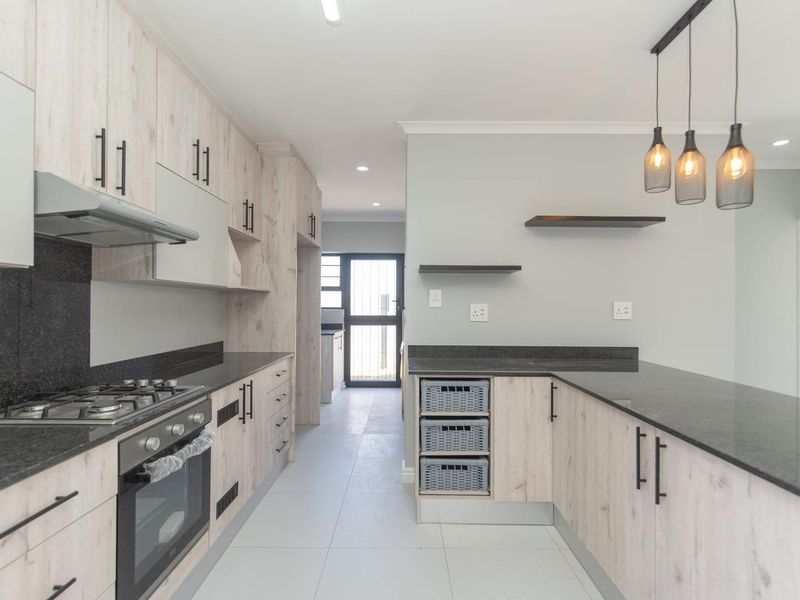 Modern kitchen featuring light wood-grain cabinetry, dark granite countertops, integrated gas hob, electric oven, and stylish pendant lighting in an open-plan layout.