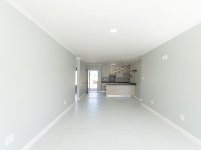 Spacious open-plan living area featuring neutral tones, tiled flooring, and a modern kitchen with built-in cabinetry and an island.
