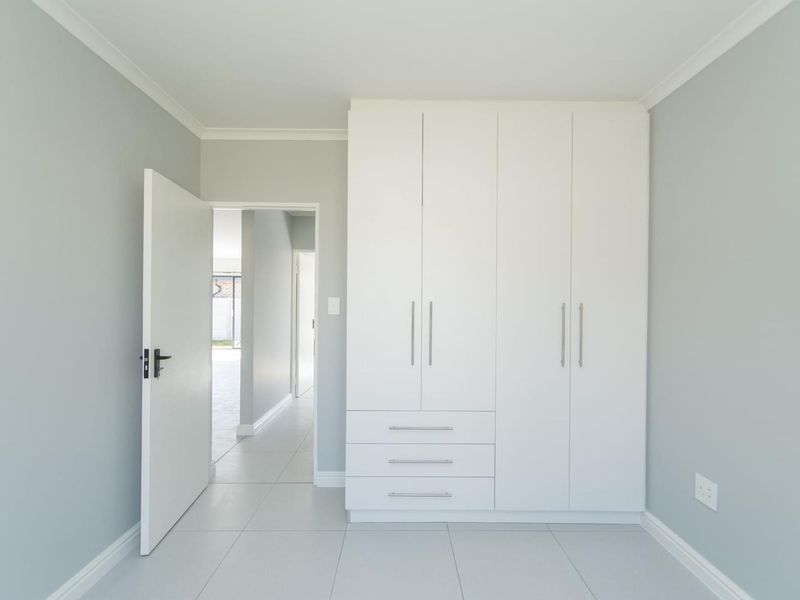 A bright, neutral bedroom featuring modern built-in cupboards, clean tiled flooring, and a seamless transition into the hallway.