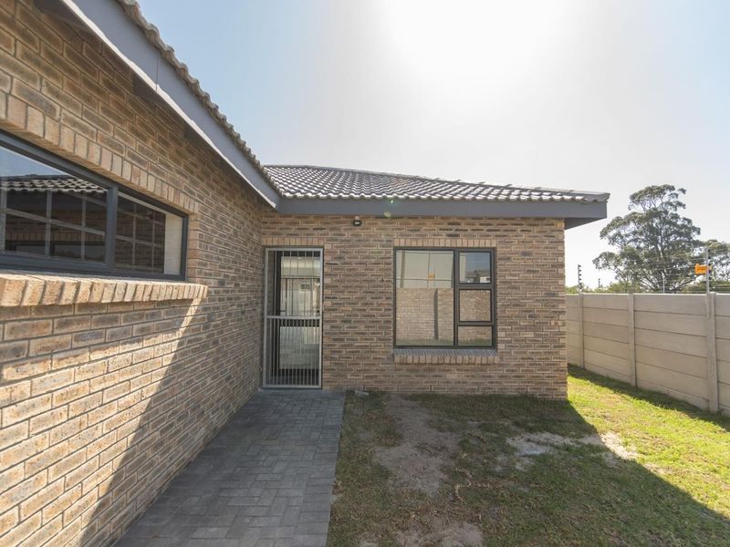 Rear view of the house featuring face brick construction, a tiled roof, paved walkway, and a secure precast concrete boundary wall.