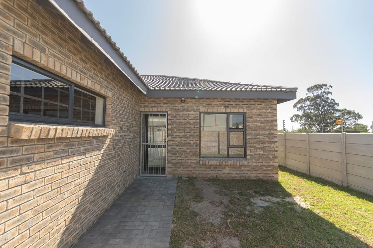 Rear view of the house featuring face brick construction, a tiled roof, paved walkway, and a secure precast concrete boundary wall.
