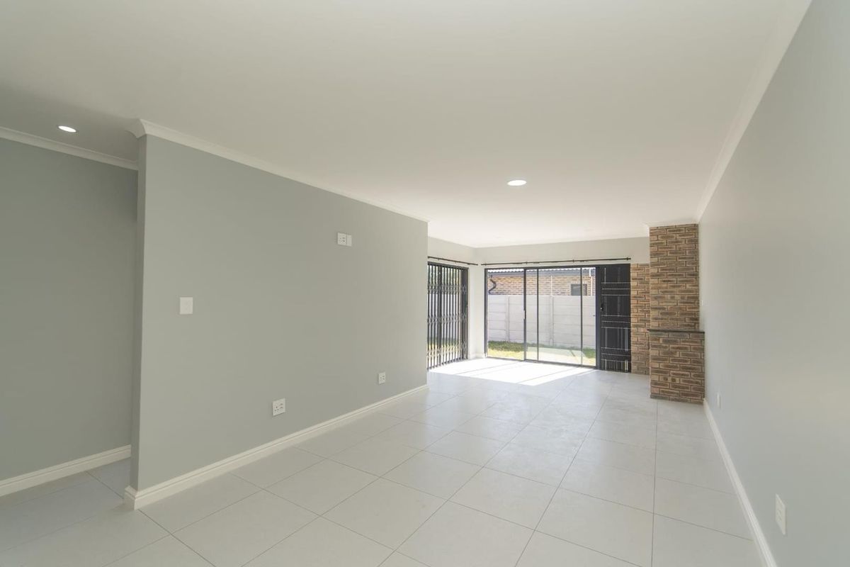 A bright, open-plan living area featuring neutral tiled flooring, recessed lighting, and a brick fireplace, with sliding glass doors leading to the exterior.