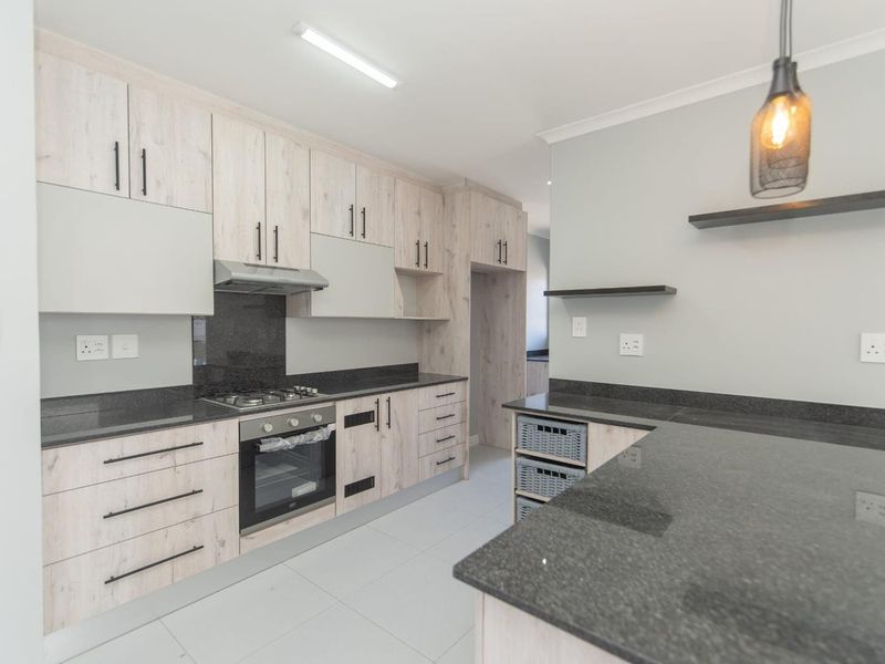 Modern kitchen featuring light wood-grain cabinetry, dark granite countertops, built-in gas hob, oven, and extractor fan with clean tiled flooring.