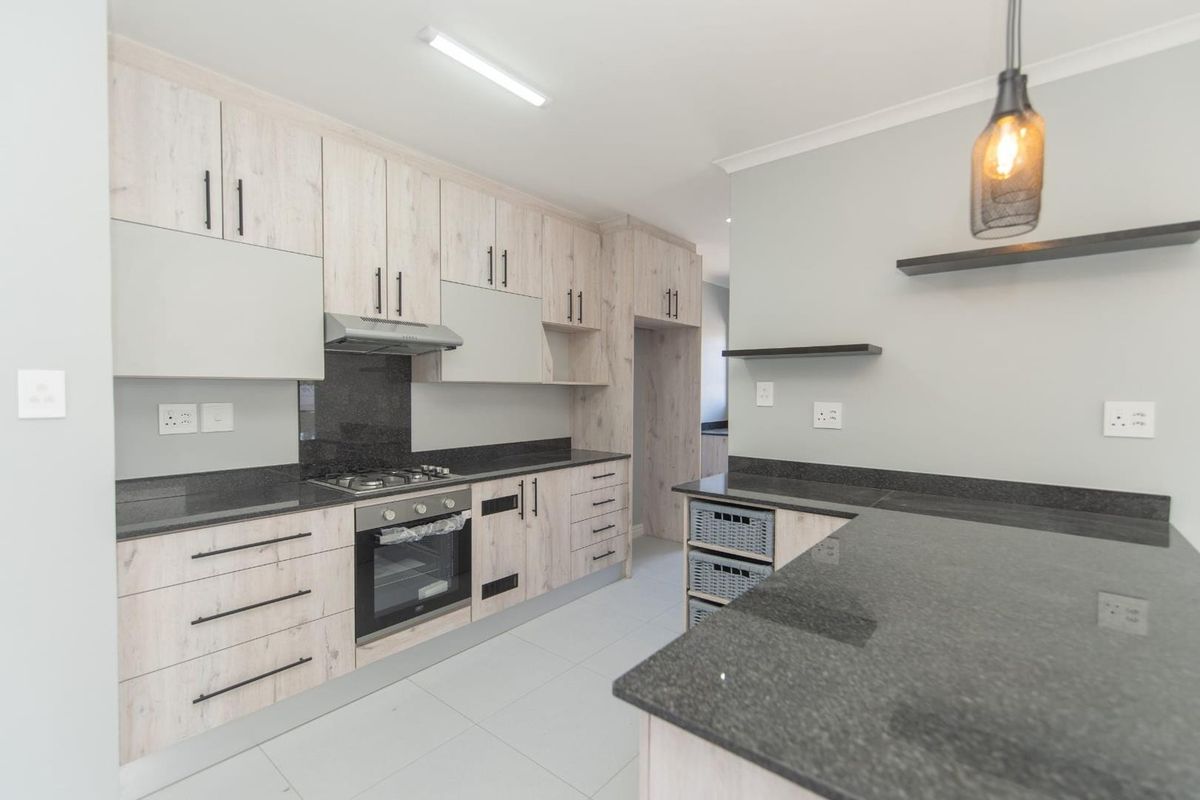 Modern kitchen featuring light wood-grain cabinetry, dark granite countertops, built-in gas hob, oven, and extractor fan with clean tiled flooring.
