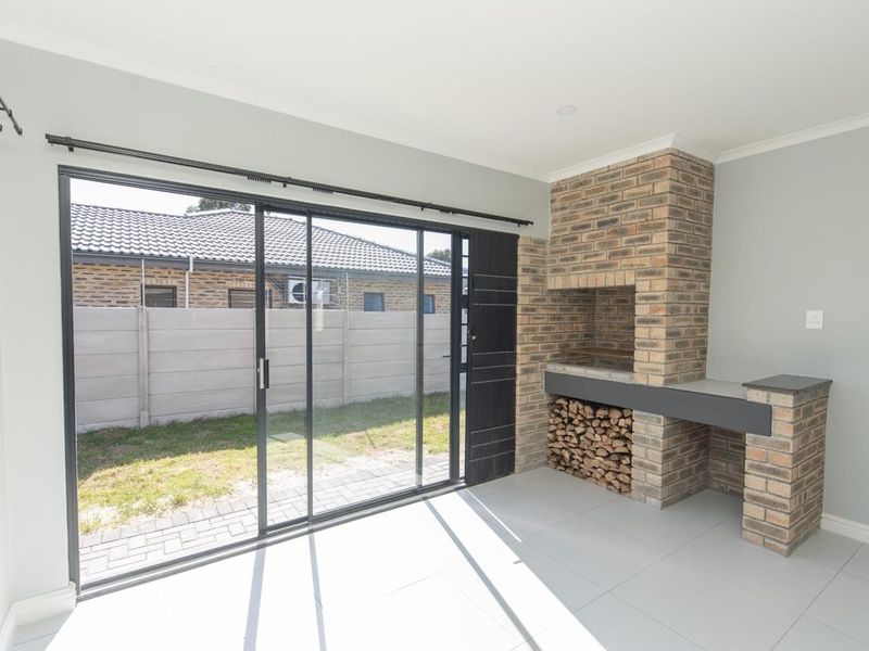 A bright, modern enclosed patio featuring a built-in brick braai, tiled flooring, and large sliding glass doors opening to the rear garden.