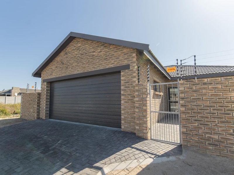 Front exterior view of a modern brick house featuring a paved driveway, secure garage door, and perimeter electric fencing.