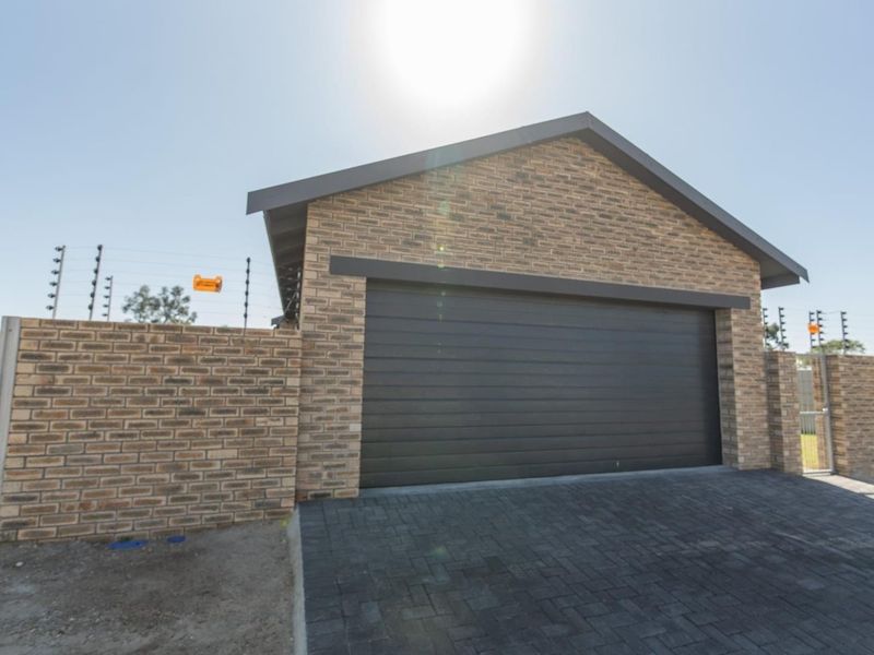 A modern brick-faced double garage featuring a dark sectional door, paved driveway, and secure perimeter wall with electric fencing.
