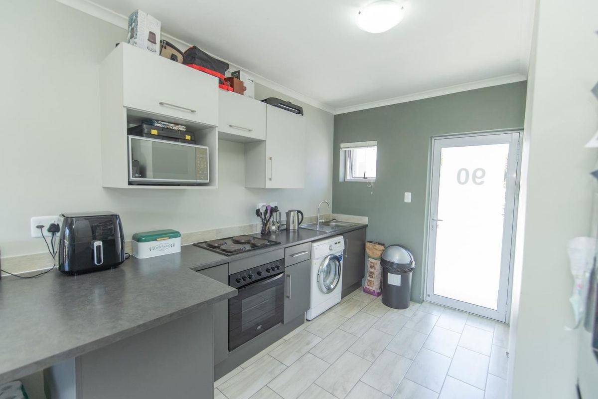 A functional kitchen featuring modern grey cabinetry, laminate countertops, built-in oven and hob, and tiled flooring with direct access to the exterior.