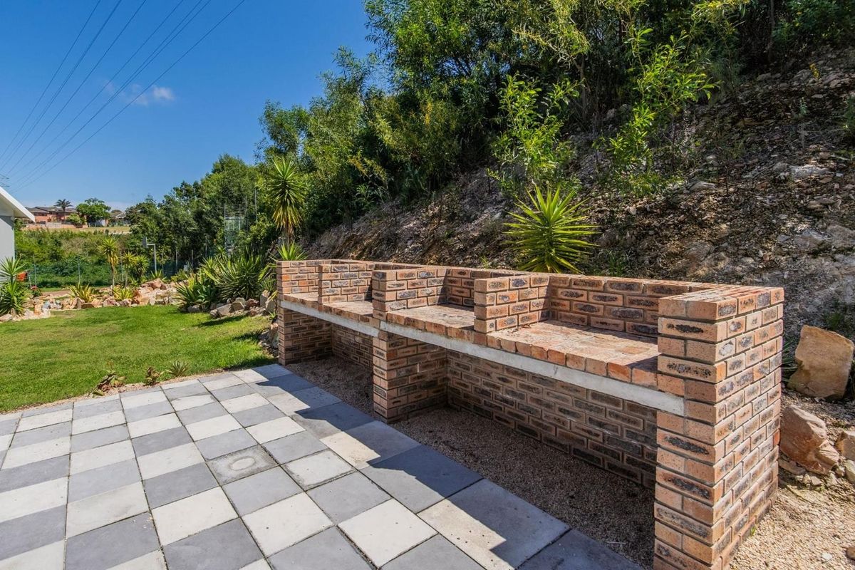 A well-maintained outdoor area featuring a large built-in brick braai and paved patio, set against a landscaped garden backdrop.