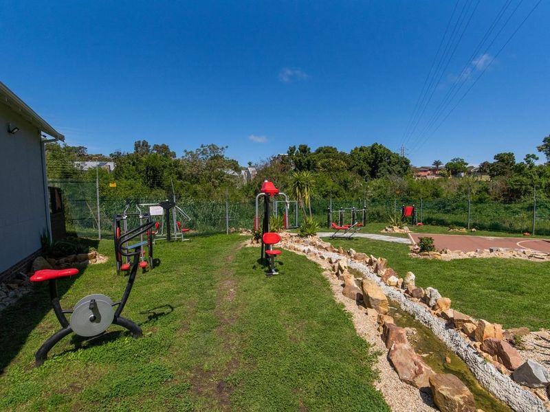 Outdoor fitness area featuring various exercise stations, a landscaped rock garden, and a paved sports court within a fenced communal space.