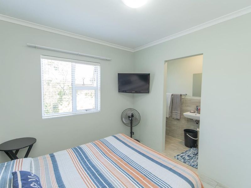 A bedroom featuring a window, wall-mounted television, and direct access to an en-suite bathroom with a vanity sink.