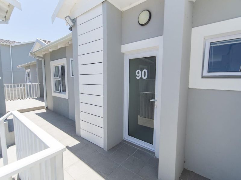 A clean and modern apartment entrance featuring a glass door, tiled walkway, and white balustrade in a well-maintained exterior setting.