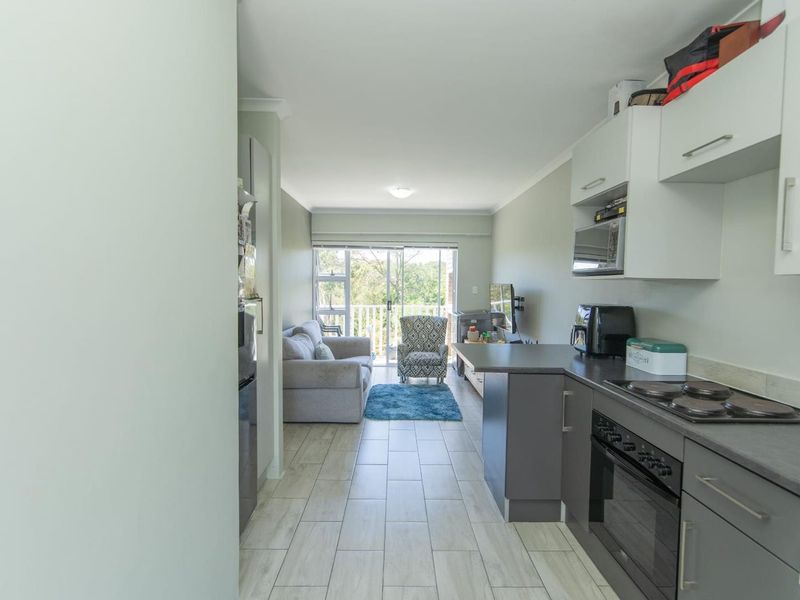 Open-plan living area featuring a modern kitchen with built-in appliances, tiled flooring, and direct access to a balcony through sliding glass doors.