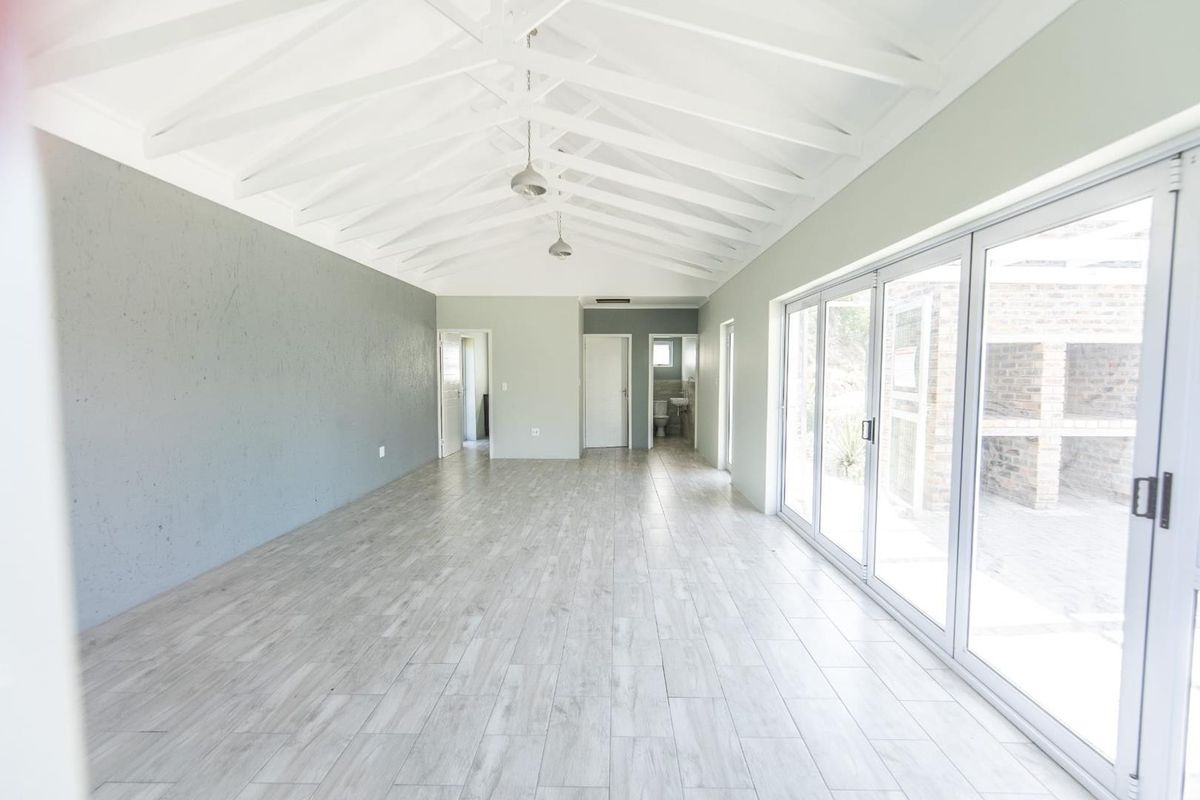 Spacious open-plan living area featuring a vaulted ceiling with exposed rafters, light wood-look tiled flooring, and large sliding glass doors leading outdoors.