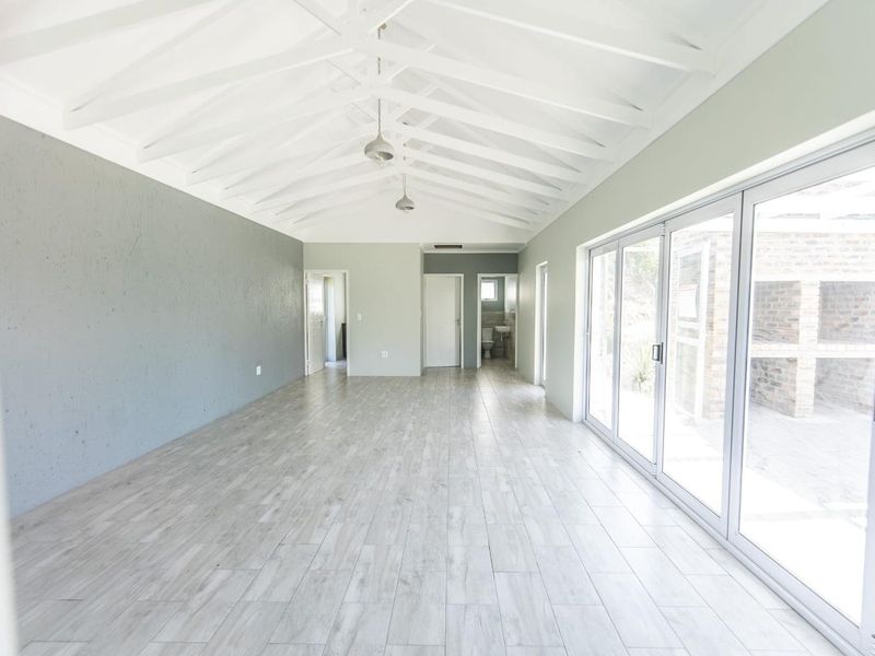 Spacious open-plan living area featuring a vaulted ceiling with exposed rafters, light wood-look tiled flooring, and large sliding glass doors leading outdoors.